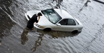 Man watches his car sitting in the flooded waters on the street.