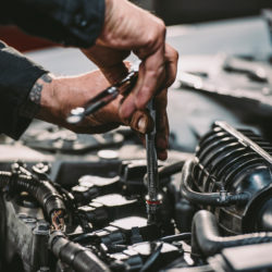 person using a ratchet, one of the tools to change spark plugs, to loosen a spark plug from the engine compartment