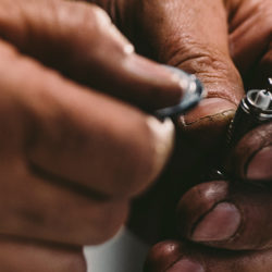 person holding a spark plug in their left hand and a gap tool in the right, preparing to gap a spark plug