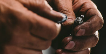 person holding a spark plug in their left hand and a gap tool in the right, preparing to gap a spark plug