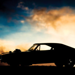 Forced induction muscle car resting on the road in the light of the setting sun. A wastegate peaks out from the top of the hood to allow compressed air to escape from this supercharged or turbocharged ride.