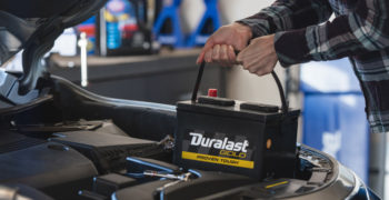 woman removing a battery from her engine compartment to demonstrate how car batteries work
